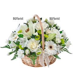 Красиво аранжирана кошница с бели цветя и зеленина, украсена с бяла панделка.