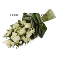Издължен букет от бели рози и обилна зеленина, привързан с панделка.