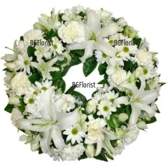 Classic funeral wreath, arranged with white flowers - lilies, carnations, chrysanthemums and a lot of greenery.