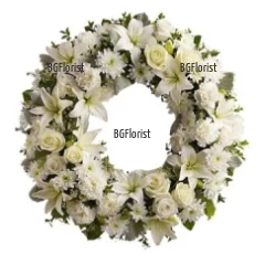 Траурен венец от бели цветя - хризантеми, лилиуми, карамфили и рози, аранжиран върху пиафлора за запазване на свежестта на цветя.