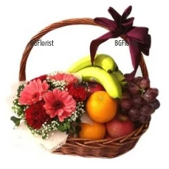 Basket, arranged with bouquet of gerberas  and carnations and various fruits.