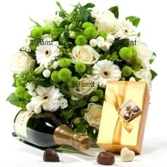 Изящен кръгъл букет от бели цветя - гербери, рози, хризантеми и зеленина, допълнен с бутилка пенливо вино и шоколадови бонбони.