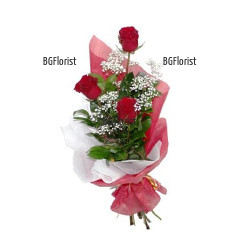 Elegant bouquet of three red roses, loving gypsophila and greenery, wrapped in gift paper.