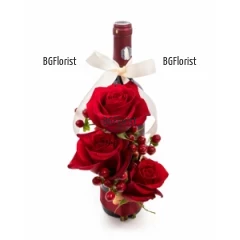 Romantic, original and modern floral arrangement of red roses, exotic hypericum, greens and a bottle of wine